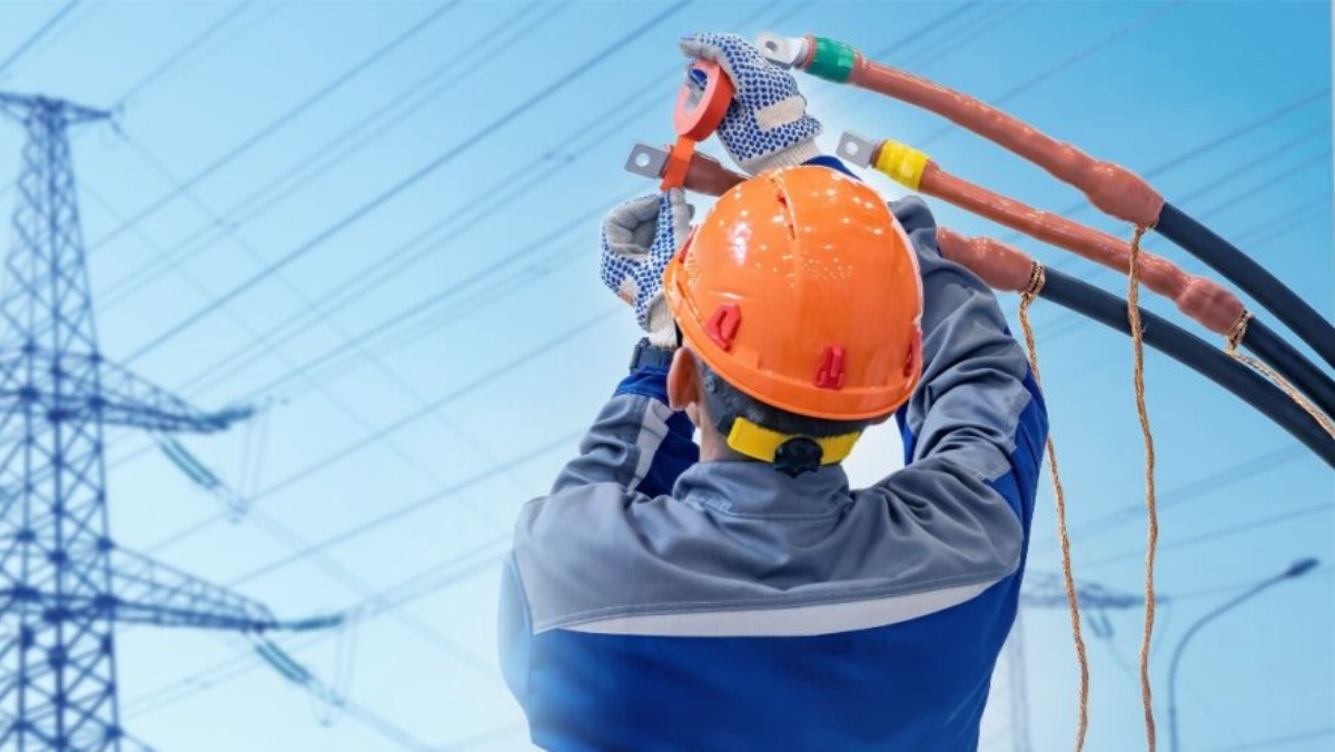 Electrical worker repairing high-voltage cables near transmission towers to support grid infrastructure