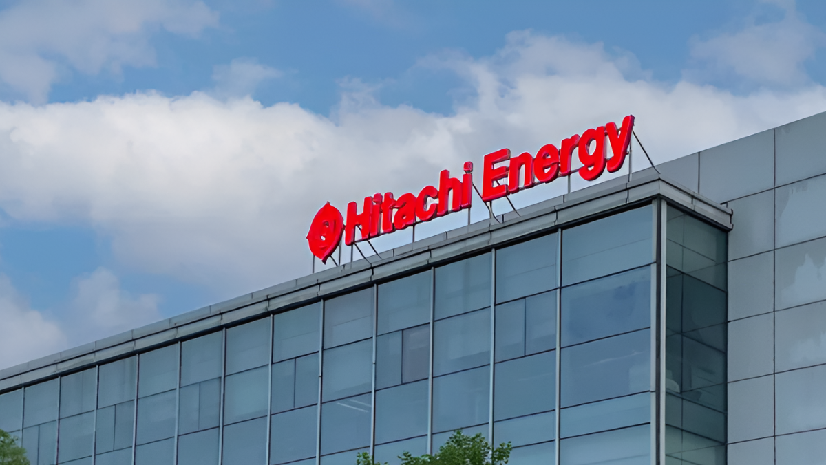 Hitachi Energy logo in bold red lettering mounted on a modern glass building under a partly cloudy sky