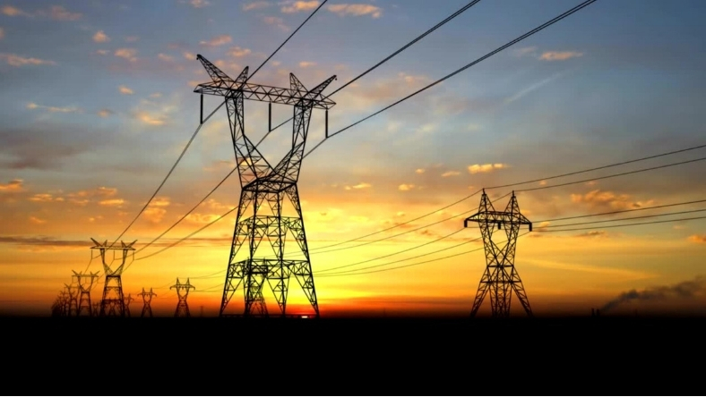 High voltage transmission lines carrying electricity across power grid at sunset